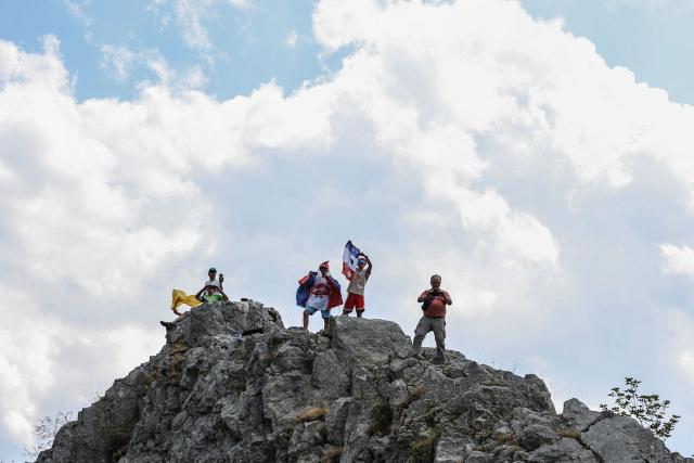 Spectators stand atop a rock formation along the roadside during the 15th stage of the 113th edition of the Tour de France cycling race, 183,9 km between Champagnole and Plateau de Solaison in the Jura mountains, on July 19, 2026. (Photo by Anne-Christine POUJOULAT / AFP)