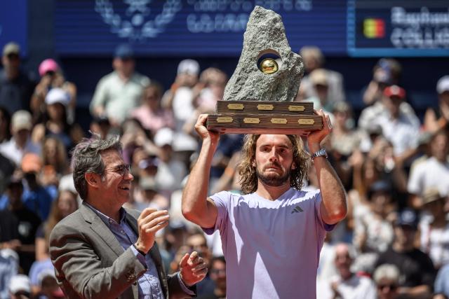 Greece's Stefanos Tsitsipas gestures as he raises the trophy next to EFG Bank CEO Giorgio Pradelli (L) following his victory against Belgium's Raphael Collignon during their men's singles final match at the Swiss Open tennis tournament in Gstaad, on July 19, 2026. (Photo by Fabrice COFFRINI / AFP)