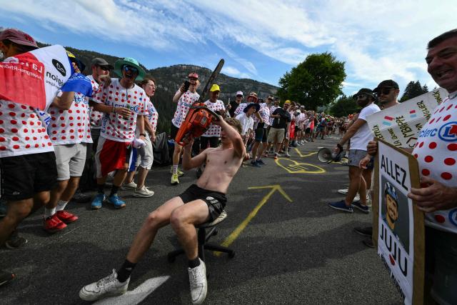 A spectator wielding a chainsaw rides a desk chair downhill as crowds await the pack of riders (peloton) in the final ascent of the 15th stage of the 113th edition of the Tour de France cycling race, 183,9 km between Champagnole and Plateau de Solaison in the Jura mountains, on July 19, 2026. (Photo by Jeff PACHOUD / AFP)