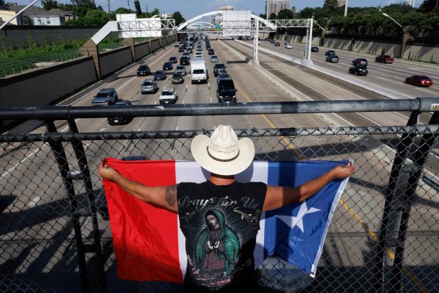 A person holds a flag on a bridge over the highway as people gather to protest the death of Mexican migrant Lorenzo Salgado Araujo, who was fatally shot by a US immmigration officer, in Houston, Texas, on July 19, 2026. The US Department of Homeland Security said on July 14 that Salgado Araujo, 52, had been the target of an operation by Immigration and Customs Enforcement (ICE) agents in Houston and had "attempted to evade arrest." Witnesses to the fatal shooting have disputed the official account of events, saying the man never tried to run over the federal officer who shot him, their lawyer said on July 17. (Photo by Mark Felix / AFP)
