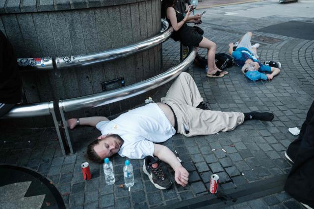 Men sleep on the ground near the Hachiko statue in Shibuya, Tokyo, in the early morning on July 20, 2026. (Photo by Yasuyoshi CHIBA / AFP)