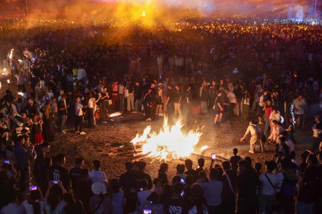 People gather around bonfires as they celebrate the Torch Festival, held by the Yi ethnic minority, in Puge County, Liangshan Prefecture, in China’s southwest Sichuan Province on July 19, 2026. The celebrations took in traditional folk activities such as horse racing, bullfighting, and dancing and singing around bonfires. (Photo by CN-STR / AFP) / China OUT