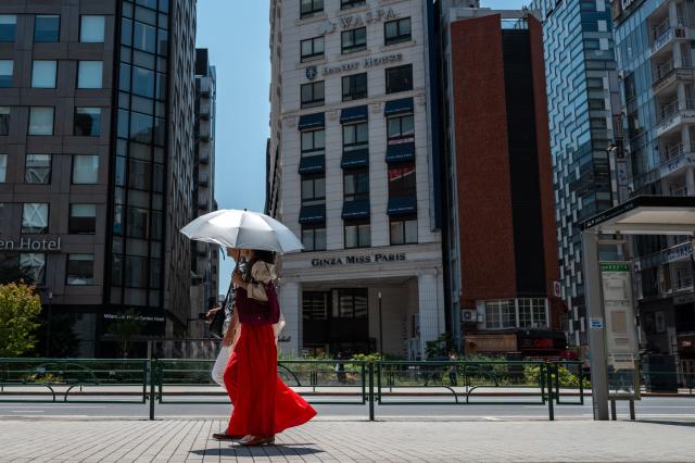 People walk with an umbrella while visiting Ginza district in Tokyo on July 20, 2026, as temperatures reach 36°C in Japan's capital. (Photo by Philip FONG / AFP)