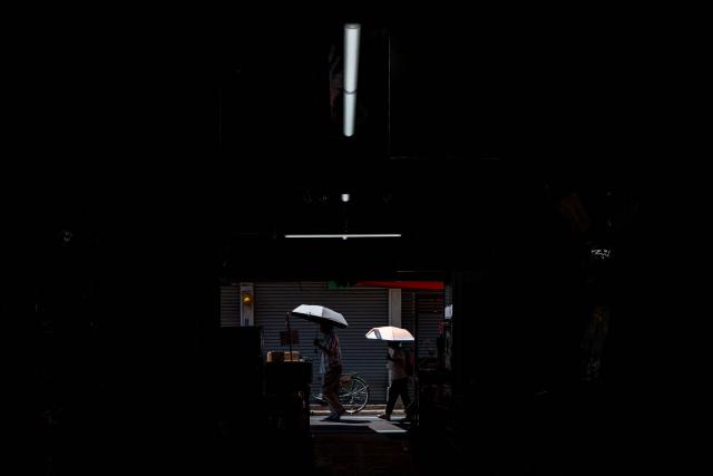People walk with umbrellas while visiting Tsukiji outer market in Tokyo on July 20, 2026, as temperatures reach 36°C in Japan's capital. (Photo by Philip FONG / AFP)