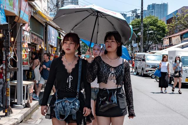People walk with an umbrella while visiting Tsukiji outer market in Tokyo on July 20, 2026, as temperatures reach 36°C in Japan's capital. (Photo by Philip FONG / AFP)