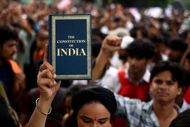 An activist and supporter of the Cockroach Janta Party (CJP) holds a copy of 'The Constitution of India' during a protest demanding the resignation of India's Education Minister Dharmendra Pradhan over alleged NEET examination irregularities in New Delhi on July 20, 2026. (Photo by Manan VATSYAYANA / AFP)