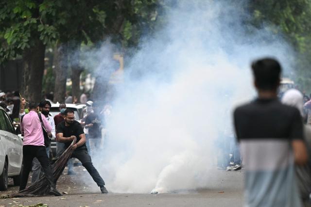Supporters of the Cockroach Janta Party (CJP) try to cover a tear gas shell with cloth during a protest demanding the resignation of India's Education Minister Dharmendra Pradhan over alleged NEET examination irregularities in New Delhi on July 20, 2026. India's riot police baton-charged protesters in New Delhi as they tried to march to parliament on July 20, escalating a protest over irregularities in major examinations. (Photo by Sajjad HUSSAIN / AFP)