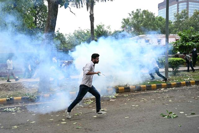 A supporter of the Cockroach Janta Party (CJP) runs as police fire tear gas shells to disperse them during a protest demanding the resignation of India's Education Minister Dharmendra Pradhan over alleged NEET examination irregularities in New Delhi on July 20, 2026. India's riot police baton-charged protesters in New Delhi as they tried to march to parliament on July 20, escalating a protest over irregularities in major examinations. (Photo by Sajjad HUSSAIN / AFP)