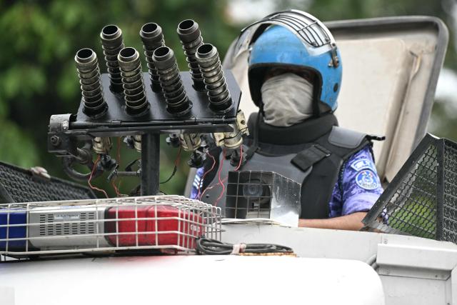 A Rapid Action Force (RAF) personnel keeps watch while standing on a multi-barrel teargas shell launching vehicle during a protest by the supporters of the Cockroach Janta Party (CJP) demanding the resignation of India's Education Minister Dharmendra Pradhan over alleged NEET exam irregularities in New Delhi on July 20, 2026. India's riot police baton-charged protesters in New Delhi as they tried to march to parliament on July 20, escalating a protest over irregularities in major examinations. (Photo by Sajjad HUSSAIN / AFP)