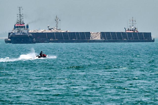 People ride personal watercraft as a tugboat tows a barge off the coast of Dubai on July 20, 2026. (Photo by AFP)