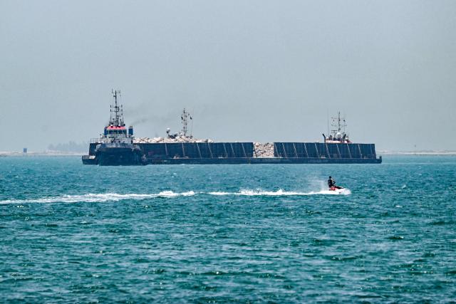 People ride personal watercraft as a tugboat tows a barge off the coast of Dubai on July 20, 2026. (Photo by AFP)