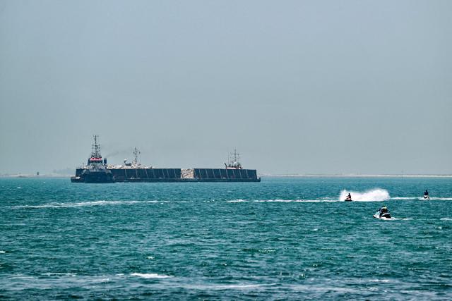 People ride personal watercraft as a tugboat tows a barge off the coast of Dubai on July 20, 2026. (Photo by AFP)