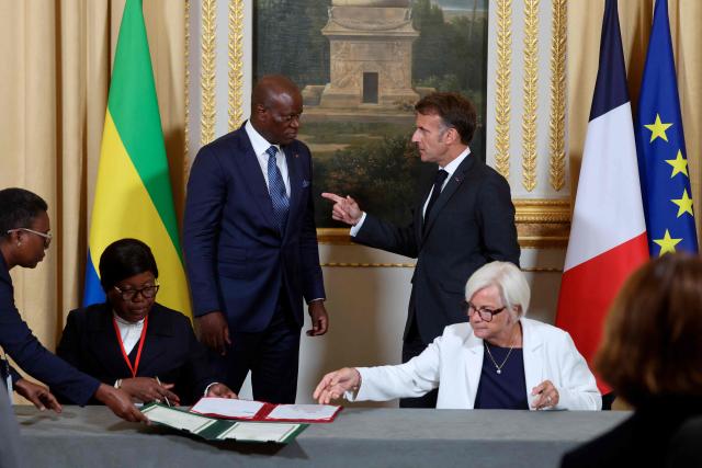 Gabon's President Brice Oligui Nguema (2ndL) and France's President Emmanuel Macron (R) talk as France's Defence Minister Catherine Vautrin and Gabon's Defence Minister Brigitte Onkanowa (L) sign documents related to the sale of the “General de Gaulle” camp on the sidelines of the state visit of Gabon's President at the Elysee Palace in Paris on July 20, 2026. (Photo by Ludovic MARIN / POOL / AFP)