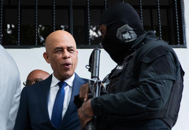 A Haitian National Police (PNH) officer from the specialized Brigade d'Opération et d'Intervention Départementale (BOID) escorts former Haitian President Michel Joseph Martelly as he leaves the Court of Appeal after giving testimony in the investigation into the July 2021 assassination of former President Jovenel Moise, in Port-au-Prince, Haiti, on July 20, 2026. Martelly, who served as the 47th President of Haiti from May 2011 to February 2016, has arrived back in Haiti. He has been summoned to give testimony as a judge examines the investigation into the July 2021 assassination of former President Jovenel Moise. (Photo by Clarens SIFFROY / AFP)