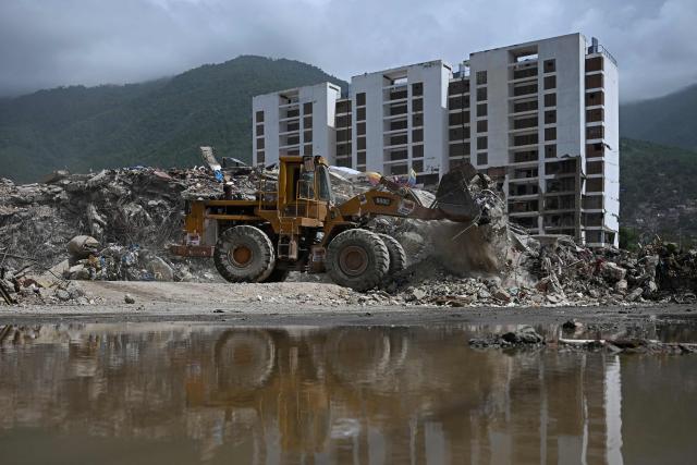 A skid-steer loader operates in front of the collapsed remains of a residential building that collapsed following the June 24, 2026 earthquakes, in Caraballeda, Venezuela, on July 20, 2026. (Photo by Federico PARRA / AFP)