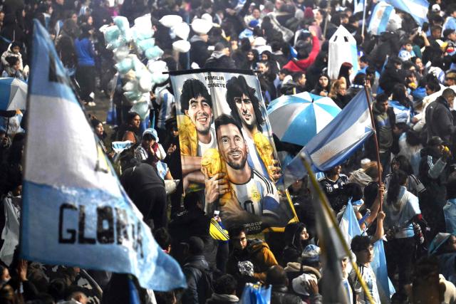 Fans hold a banner depicting Argentine football legends Diego Maradona, Mario Kempes and Lionel Messi holding FIFA World Cup trophies as supporters gather near the Argentine Football Association (AFA) training camp in Ezeiza, Buenos Aires Province, on July 20, 2026, while awaiting the arrival of Argentina's national football team from the United States following its defeat in the 2026 FIFA World Cup final. (Photo by Luis ROBAYO / AFP)