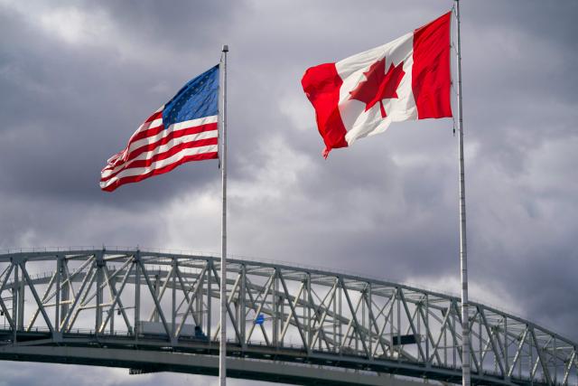 (FILES) The US and Canada flags flutter next to the Blue Water Bridge border crossing in Point Edward, Ontario, on October 24, 2025. President Donald Trump signed orders July 20, to impose new 50-percent tariffs on many Canadian goods, claiming "discriminatory treatment" by Ottawa against American alcohol, automobile and dairy products. The tariffs will take effect in 30 days and cover a range of items including wine, hockey sticks and cement, according to a White House fact sheet. Trump, who saw many of his tariffs struck down by the Supreme Court earlier this year, tapped an untested legal provision for the new duties -- Section 338 of the Tariff Act of 1930. (Photo by Geoff Robins / AFP)