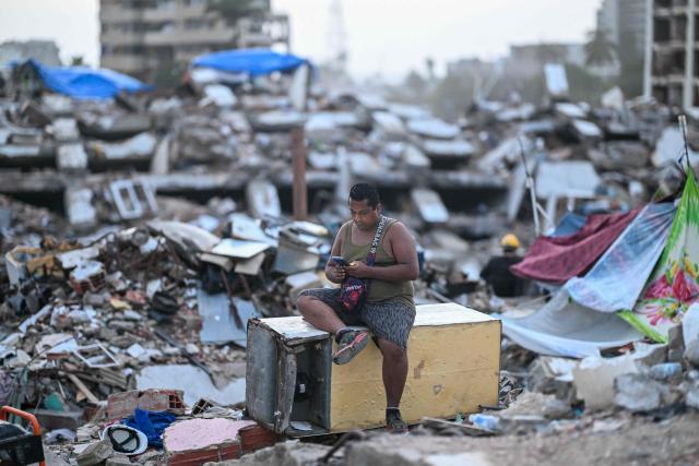 A man sits on top of a refrigerator amid the rubble of a residential building that collapsed following the June 24 earthquakes, in Caraballeda, Venezuela, on July 20, 2026. The number of people killed in the powerful dual Venezuela earthquakes last month rose to 5,278, according to official figures updated Monday. The June 24 earthquakes, which recorded magnitudes of 7.2 and 7.5, profoundly impacted the north of the country, particularly the coastal state of La Guaira, near the capital Caracas. (Photo by Juan BARRETO / AFP)