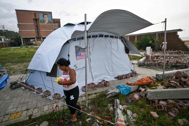 A woman walks past a tent with a US flag in Catia La Mar, Venezuela, on July 20, 2026. The number of people killed in the powerful dual Venezuela earthquakes last month rose to 5,278, according to official figures updated Monday. The June 24 earthquakes, which recorded magnitudes of 7.2 and 7.5, profoundly impacted the north of the country, particularly the coastal state of La Guaira, near the capital Caracas. (Photo by Juan BARRETO / AFP)