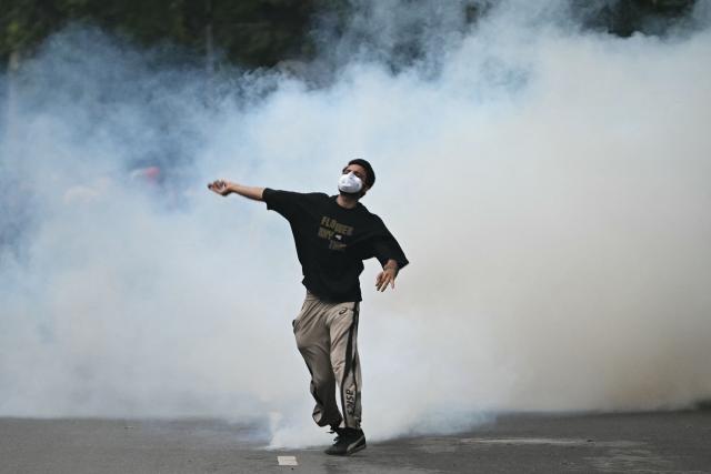 A protester throws back a tear gas canister fired by Rapid Action Force (RAF) personnel to disperse supporters of the Cockroach Janta Party (CJP), during a protest demanding the resignation of India's Education Minister Dharmendra Pradhan over alleged NEET exam irregularities in New Delhi on July 20, 2026. Indian police fired tear gas and baton-charged protesters in New Delhi on July 20 as they tried to march on parliament to demand the resignation of the education minister over irregularities in major examinations. (Photo by Arun SANKAR / AFP)