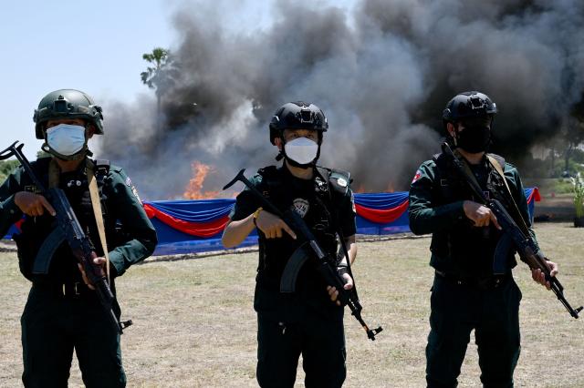 Police officers stand guard in front of smoke rising from burning drugs during a destruction ceremony to mark the UN's "International Day against Drug Abuse and Illicit Trafficking" in Kandal province on July 21, 2026. (Photo by TANG CHHIN Sothy / AFP)
