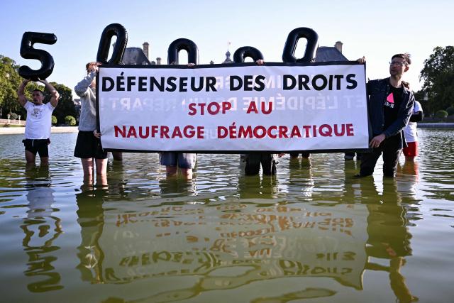 Protestors hold a banenr reading "Human Rights Defender: stop the democratic sinking", during a gathering organised by French association AIDES and Sidaction against the appointment of the new Human Rights Defender by senators at the Jardin du Luxembourg, in Paris on July 21, 2026. (Photo by Lou BENOIST / AFP)