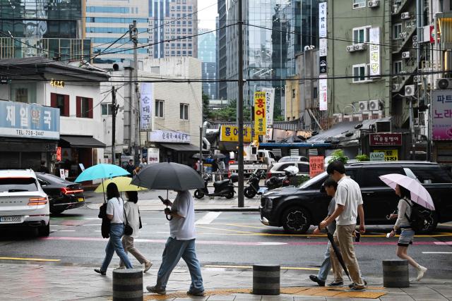 People carry umbrellas as they walk along a sidewalk in Seoul on July 21, 2026. (Photo by GREG BAKER / AFP)
