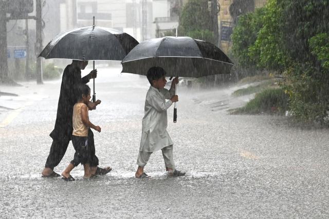 Children hold umbrellas whilst crossing a street as it rains in Peshawar, in Pakistan's Khyber Pakhtunkhwa province on July 21, 2026. (Photo by Abdul MAJEED / AFP)