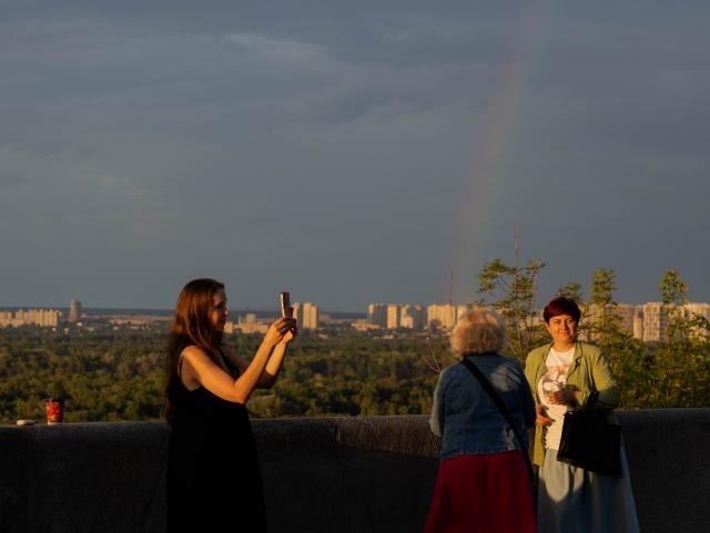 A woman takes a photograph from an observation platform in the Podil district after a rain shower, in Kyiv on July 21, 2026, amid the Russian invasion of Ukraine. (Photo by Tetiana DZHAFAROVA / AFP)