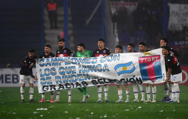 Tigre players hold a banner reading "Champions are those who never give up... Thank you national team" in tribute to the Argentina national football team and its FIFA World Cup 2026 campaign ahead of the first leg of the Copa Sudamericana knockout round play-off football match between Uruguay's Nacional and Argentina's Tigre at the Gran Parque Central satdium in Montevideo, on July 21, 2026. (Photo by Dante FERNANDEZ / AFP)