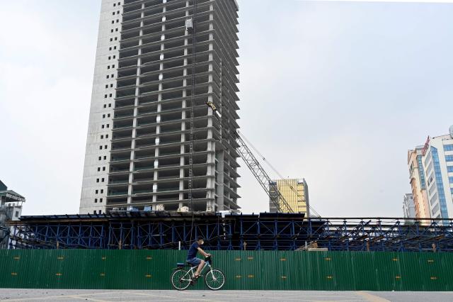A man cycles past a construction site in Hanoi on July 22, 2026. (Photo by Nhac NGUYEN / AFP)