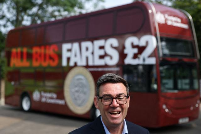 Britain's Prime Minister Andy Burnham reacts in front of a FirstGroup bus at the bus station during an interview in Bath, western England, on July 22, 2026. Burnham, who became prime minister on July 20, pledged on July 22 to ease cost-of-living pressures, unveiling a tax cut on household electricity prices and a £2 (2.70 USD) cap on single bus fares in his first days in the job. (Photo by Toby Melville / POOL / AFP)