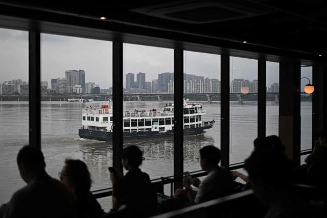 People watch from a ferry terminal as a cruise boat passes by on the Han River in Seoul on July 22, 2026. (Photo by GREG BAKER / AFP)