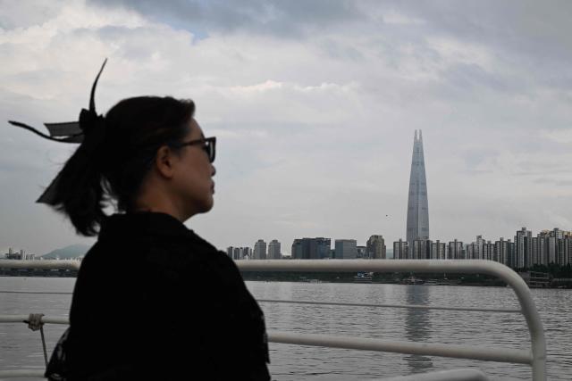 A woman rides on a ferry on the Han River as the Lotte World Tower is seen behind in Seoul on July 22, 2026. (Photo by GREG BAKER / AFP)
