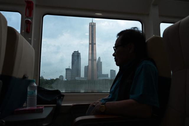 A man rests on a ferry as it passes by the Hanwha building beside the Han River in Seoul on July 22, 2026. (Photo by GREG BAKER / AFP)