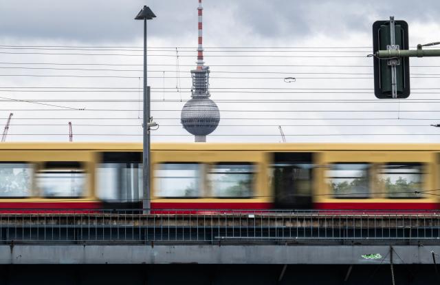 An S-Bahn train pulls into an elevated S-Bahn station operated by German railway giant Deutsche Bahn, with the Berlin TV Tower (Fernsehturm) in the background in Berlin on a cloudy chilly summer day, on July 22, 2026. (Photo by John MACDOUGALL / AFP)