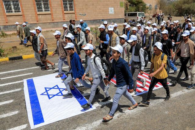 University students walk over depictions of the Israeli and UK flags while marching in a demonstration to show their support for the Houthi movement amid escalating tensions with Saudi Arabia, at the Sanaa University campus in Yemen's Houthi-held capital Sanaa on July 22, 2026. Yemen's Houthis had on July 20 announced a maritime embargo of Saudi Arabia, stepping up the US-Iran war as the rebels threatened the top oil exporter's ability to bypass the Strait of Hormuz. The US president has responded that he would "take care of" them if they followed through. (Photo by Mohammed HUWAIS / AFP) / 