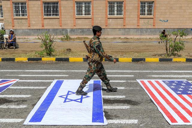 A fighter loyal to Yemen's Houthi movement walks over depictions of the Israeli and US during a demonstration by university students to show their support for the Houthis amid escalating tensions with Saudi Arabia, at the Sanaa University campus in the Houthi-held capital Sanaa on July 22, 2026. Yemen's Houthis had on July 20 announced a maritime embargo of Saudi Arabia, stepping up the US-Iran war as the rebels threatened the top oil exporter's ability to bypass the Strait of Hormuz. The US president has responded that he would "take care of" them if they followed through. (Photo by Mohammed HUWAIS / AFP) / 