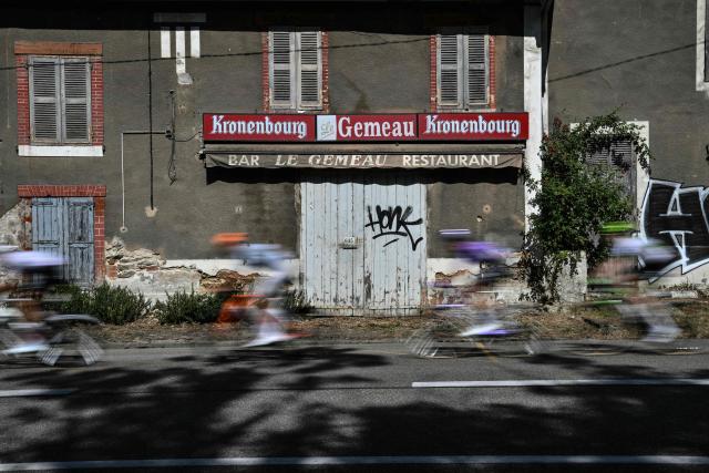 Riders cycle past a closed bar during the 17th stage of the 113th edition of the Tour de France cycling race, 174,7 km between Chambéry and Voiron in the French Alps, on July 22, 2026. (Photo by Jeff PACHOUD / AFP)