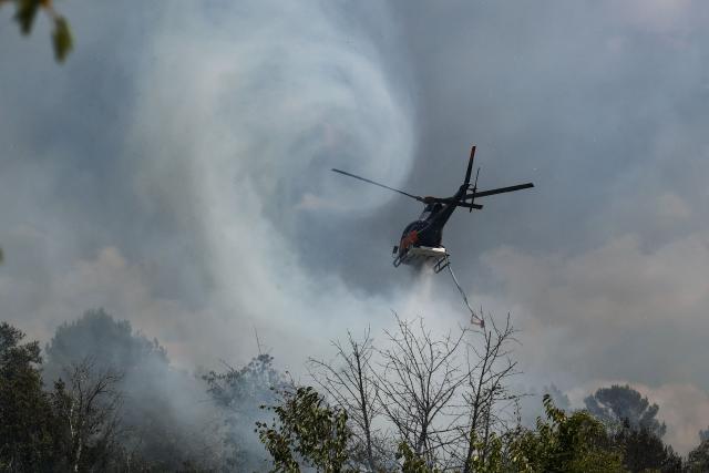 A helicopter drops water over a burning area as a wildfire flares up again in Ponteves, southeastern France on July 22, 2026. Firefighters have managed to contain the fierce blaze that swept through 2,550 hectares in the Var in less than a day, forcing the evacuation of around 500 people, and which on July 22, 2026 is still burning across a vast mountainside. (Photo by Thibaud MORITZ / AFP)