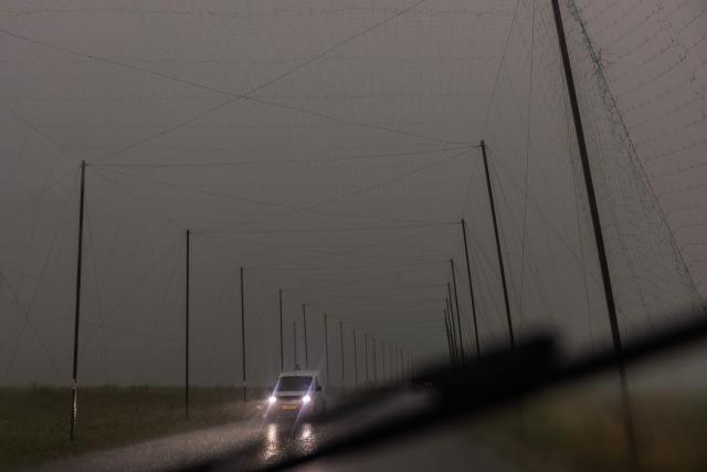 A car drives through heavy rain along a road covered with anti-drone nets, in the Kharkiv region on July 21, 2026, amid the Russian invasion of Ukraine. (Photo by Roman PILIPEY / AFP)