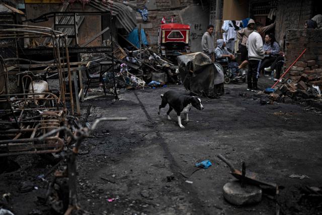 People and a dog remain near debris at the site of a fire that killed ten people in Lima on July 22, 2026. A fire in a low-income neighborhood in Lima killed 10 people and destroyed two homes, Peru's civil defense reported. Two more people were injured, the INDECI civil defense institute wrote in a social media post. (Photo by ERNESTO BENAVIDES / AFP)