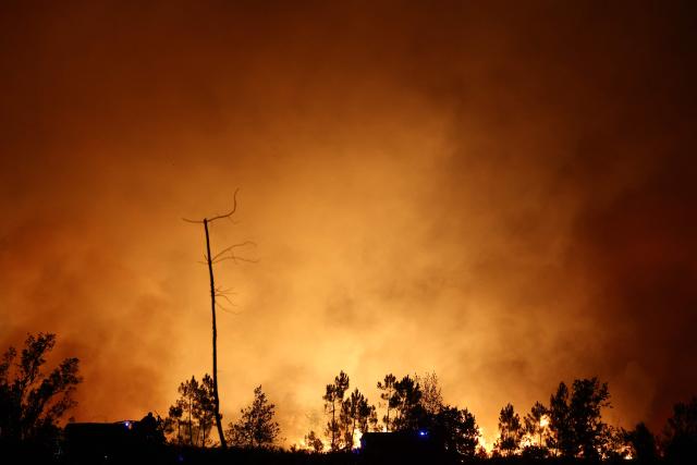 This photograph shows a wooden area engulfed in flames during a wildfire in Le Porge, south-western France on July 22, 2026. A fast-moving wildfire has burned 900 hectares north of Arcachon Bay in southwestern France, forcing the evacuation of more than 4,000 residents and tourists. The blaze, described by firefighters as exceptionally intense, spread sixfold in less than three hours through dense pine forests and is now advancing toward Ares and Lege-Cap-Ferret. The area was previously devastated by major wildfires in 2022. (Photo by ROMAIN PERROCHEAU / AFP)