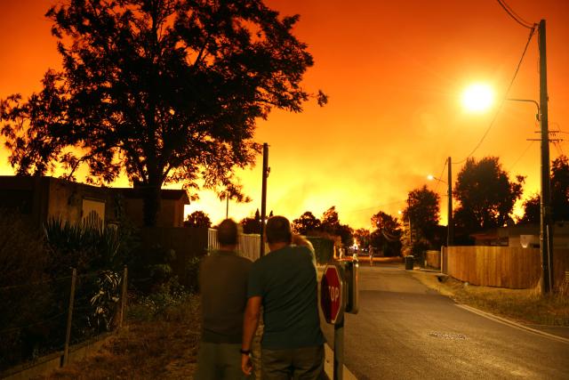 Residents look at the sky illuminated by wildfires in Le Porge, south-western France early on July 23, 2026. A fast-moving wildfire has burned 900 hectares north of Arcachon Bay in southwestern France, forcing the evacuation of more than 4,000 residents and tourists. The blaze, described by firefighters as exceptionally intense, spread sixfold in less than three hours through dense pine forests and is now advancing toward Ares and Lege-Cap-Ferret. The area was previously devastated by major wildfires in 2022. (Photo by ROMAIN PERROCHEAU / AFP)