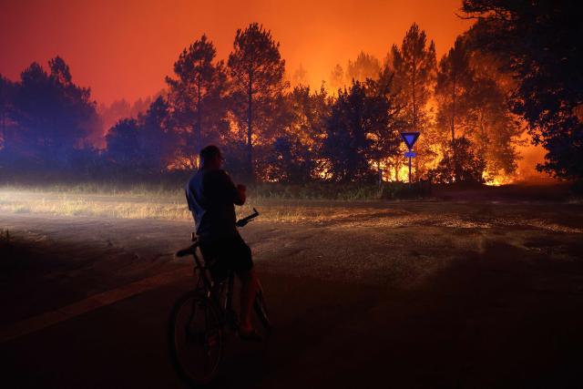 A resident looks at the approaching wildfire in Le Porge, south-western France early on July 23, 2026. A fast-moving wildfire has burned 900 hectares north of Arcachon Bay in southwestern France, forcing the evacuation of more than 4,000 residents and tourists. The blaze, described by firefighters as exceptionally intense, spread sixfold in less than three hours through dense pine forests and is now advancing toward Ares and Lege-Cap-Ferret. The area was previously devastated by major wildfires in 2022. (Photo by ROMAIN PERROCHEAU / AFP)