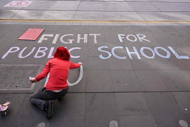 A person writes a slogan on the pavement as teachers march through Melbourne's city centre to protest over pay and conditions on July 23, 2026. Tens of thousands of public school teachers went on strike following a pay dispute with the state government, closing or disrupting some 500 state schools. (Photo by William WEST / AFP)