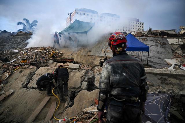 A rescue team works as a man sprays pesticides on the rubble of a building in Caraballeda, Venezuela, on July 22, 2026, nearly a month after the June 24 earthquakes. The number of people killed in the powerful dual Venezuela earthquakes last month rose to 5,278, according to official figures updated on July 20, 2026. (Photo by Juan BARRETO / AFP)
