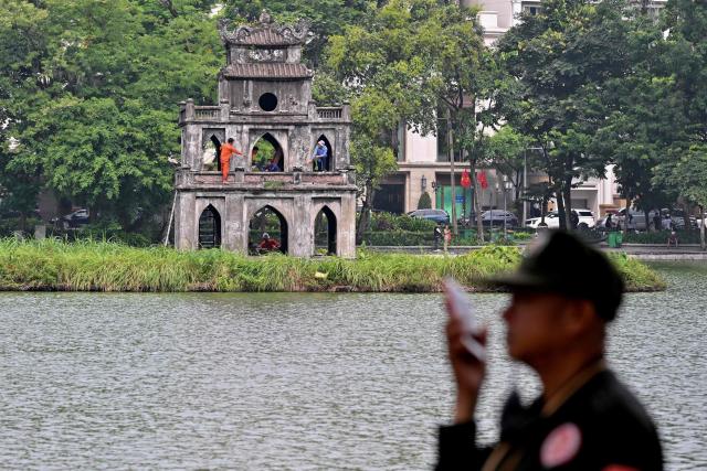 A security guard uses his phone while workers renovate the "Thap Rua" (Tower of the Turtle) at Hoan Kiem Lake in Hanoi on July 23, 2026. (Photo by Nhac NGUYEN / AFP)