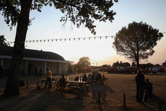 Inhabitants sit outside before taking a breakfast with firefighters outside the Gerard Blanc festival hall in Le Porge, southwestern France on July 23, 2026, following a wildfire and the evacuation of the residents. A highly virulent wildfire has swept through more than 2,000 hectares since July 22, 2026 near the Arcachon Basin (Gironde), where nearly 12,000 residents and tourists have been evacuated in total from this area of the Landes de Gascogne forest, already devastated by flames in 2022. (Photo by ROMAIN PERROCHEAU / AFP)