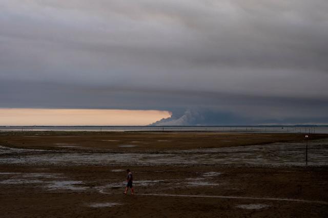 This picture shows a man walking at low tide on the beach in Andernos-Les Bains during a forest fire in Biscarosse forest, southwestern France, on July 23, 2026, as part of the nearby area has been evacuated. A highly virulent wildfire has swept through more than 2000 hectares since July 23, 2026 southern the Arcachon Basin (Gironde), from this area of the Landes de Gascogne forest, already devastated by flames in 2022. (Photo by Olivier MORIN / AFP)